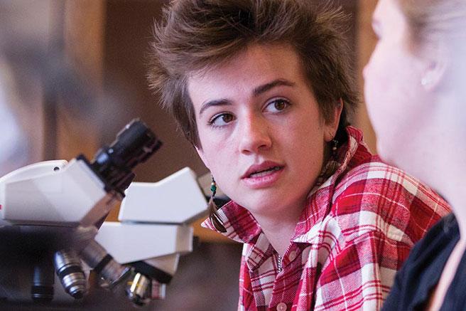 Student in class with microscope talking to professor