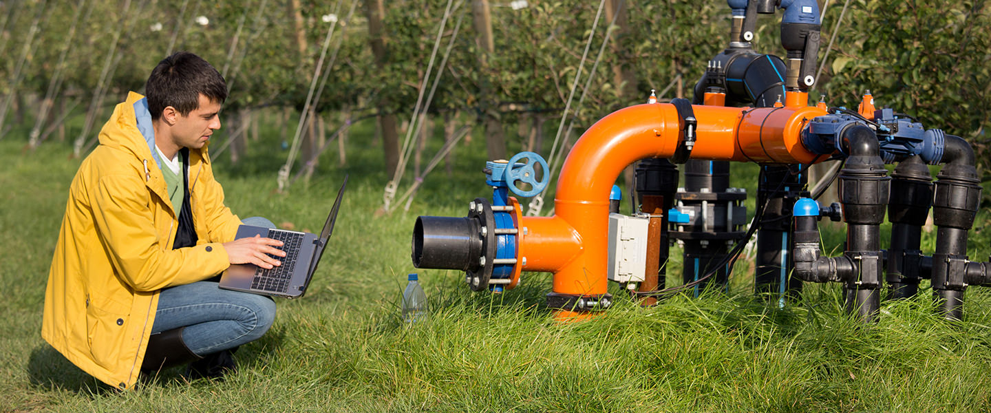 A man with a lap top examines water pipes. 