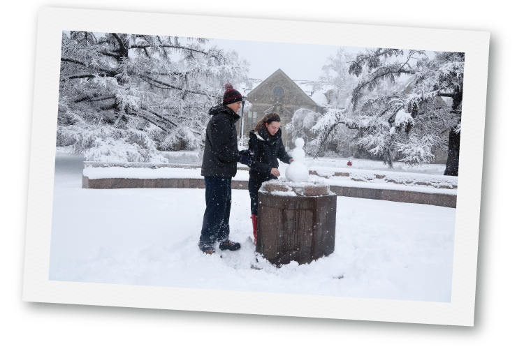 Two students building a snowman together outside in the winter