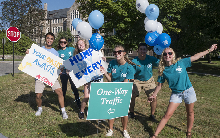 As cars roll onto campus, students cheer and wave signs. 