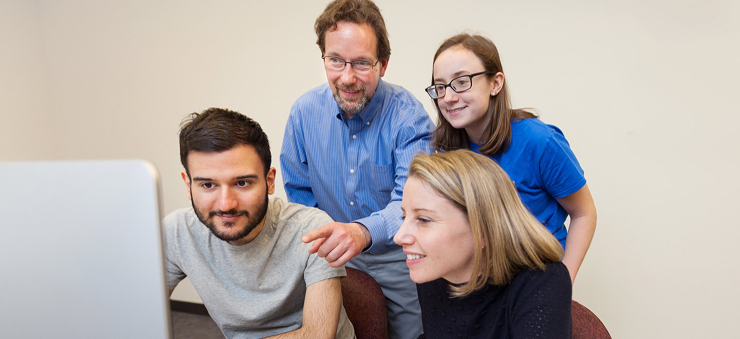 Three Pathways students and a professor look at a computer screen