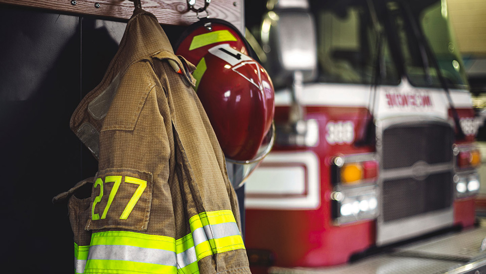 A firefighter uniform and hat hang with a fire truck in the background