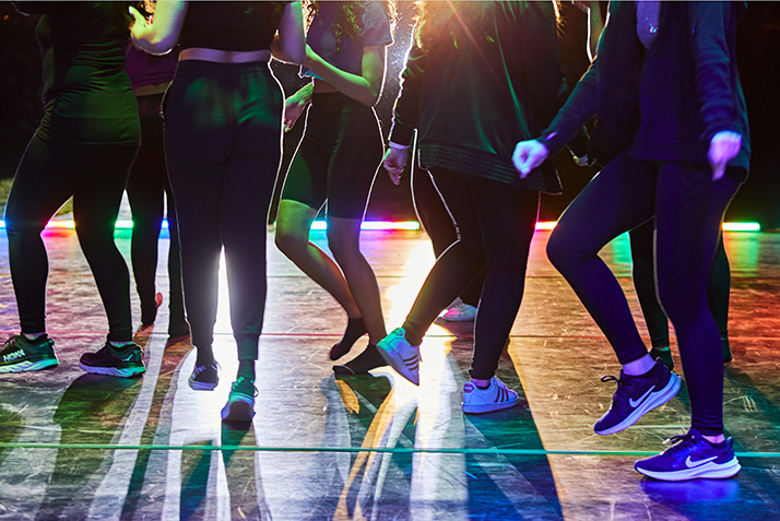 A close up of dancers' feet as they perform against brightly colored lights. 