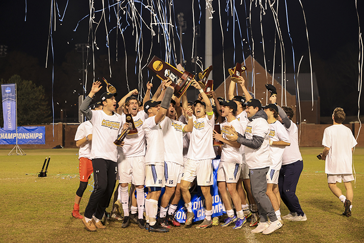 The team hoists the trophy as confetti falls on them.