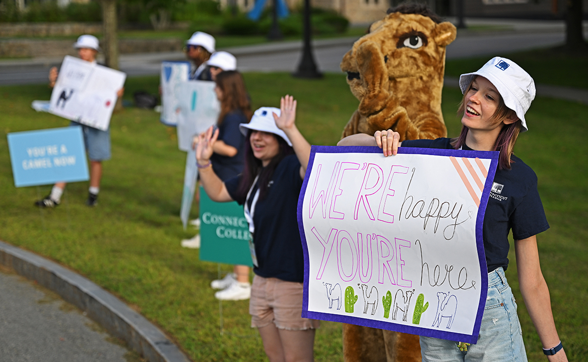 Students and the Camel mascot welcome families driving onto campus.