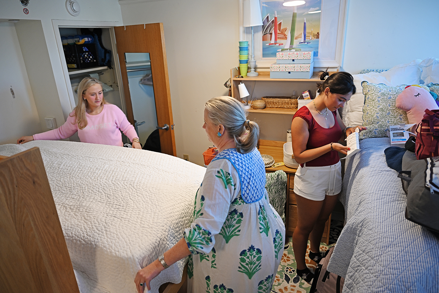 A student makes a bed with the help of her mother while another unpacks in their new dorm room