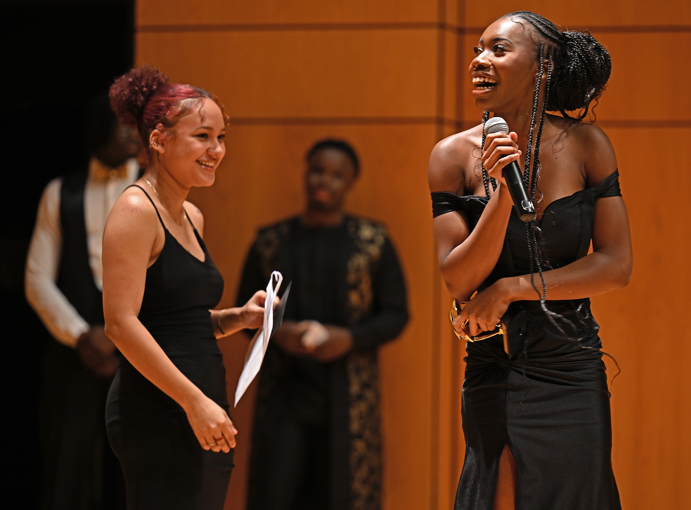 smiling student with microphone looks back at student who just presented her with award