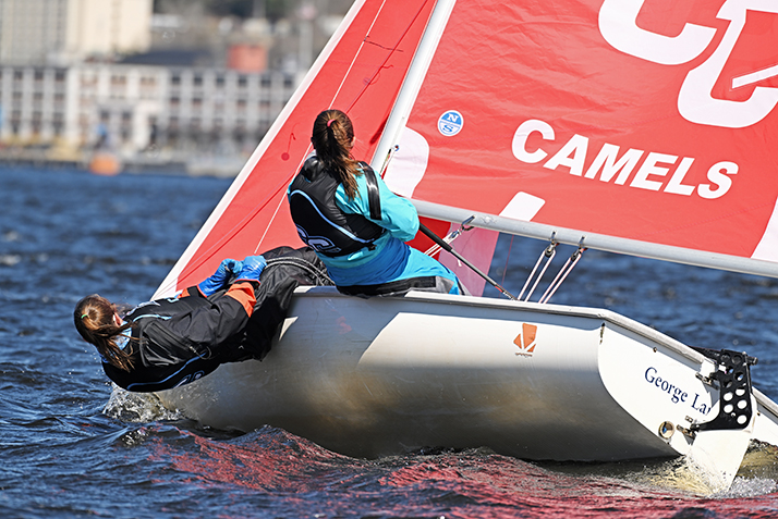 two sailors hike out over the side of their boat making a turn