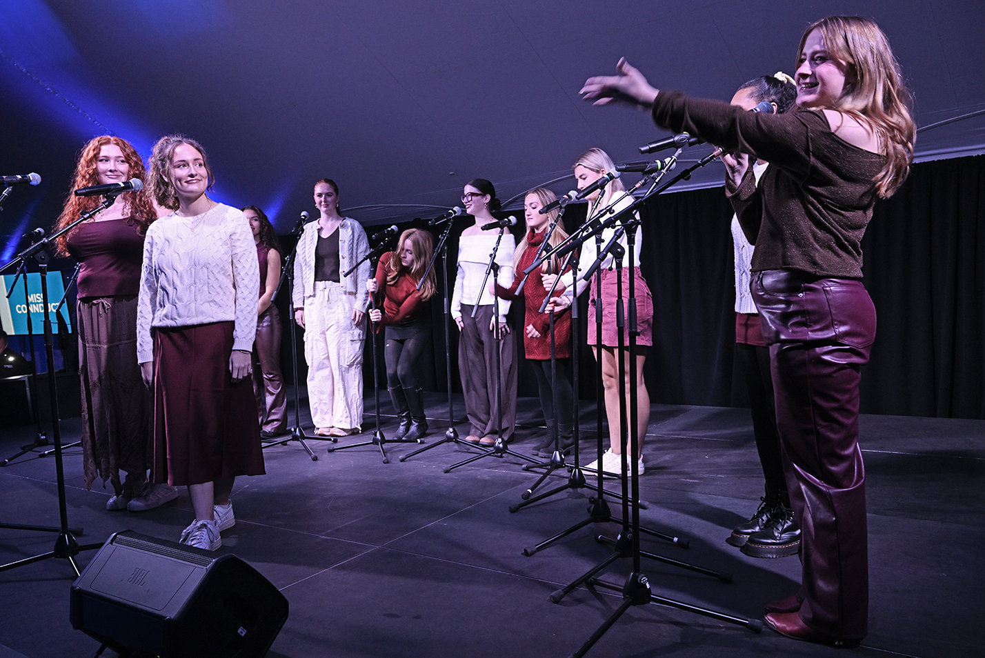 The leader of an a cappella group introduces the two soloists for a song on stage.