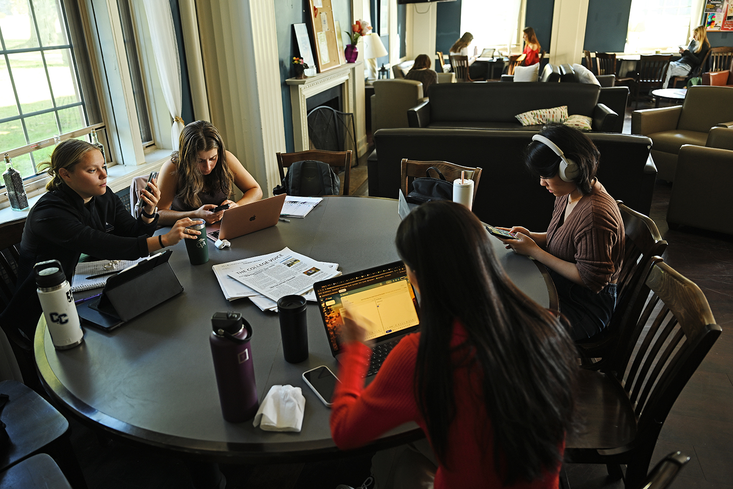 A group of students sit at a large circular table drinking coffee and studying.