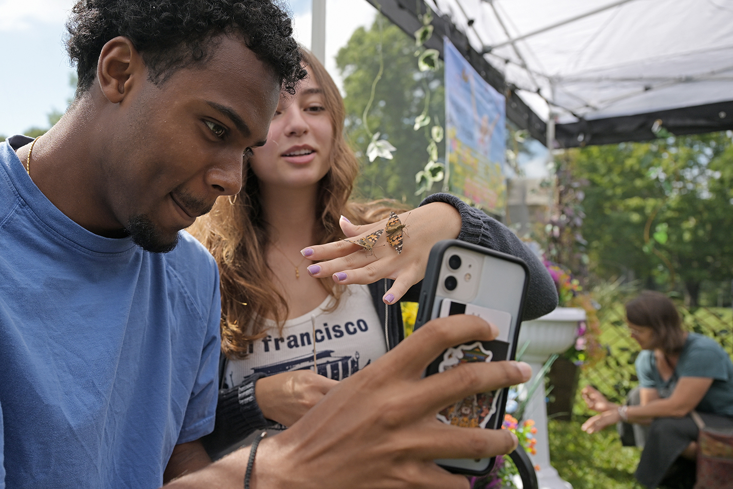 one student takes a photo of another with butterflies on her hand.