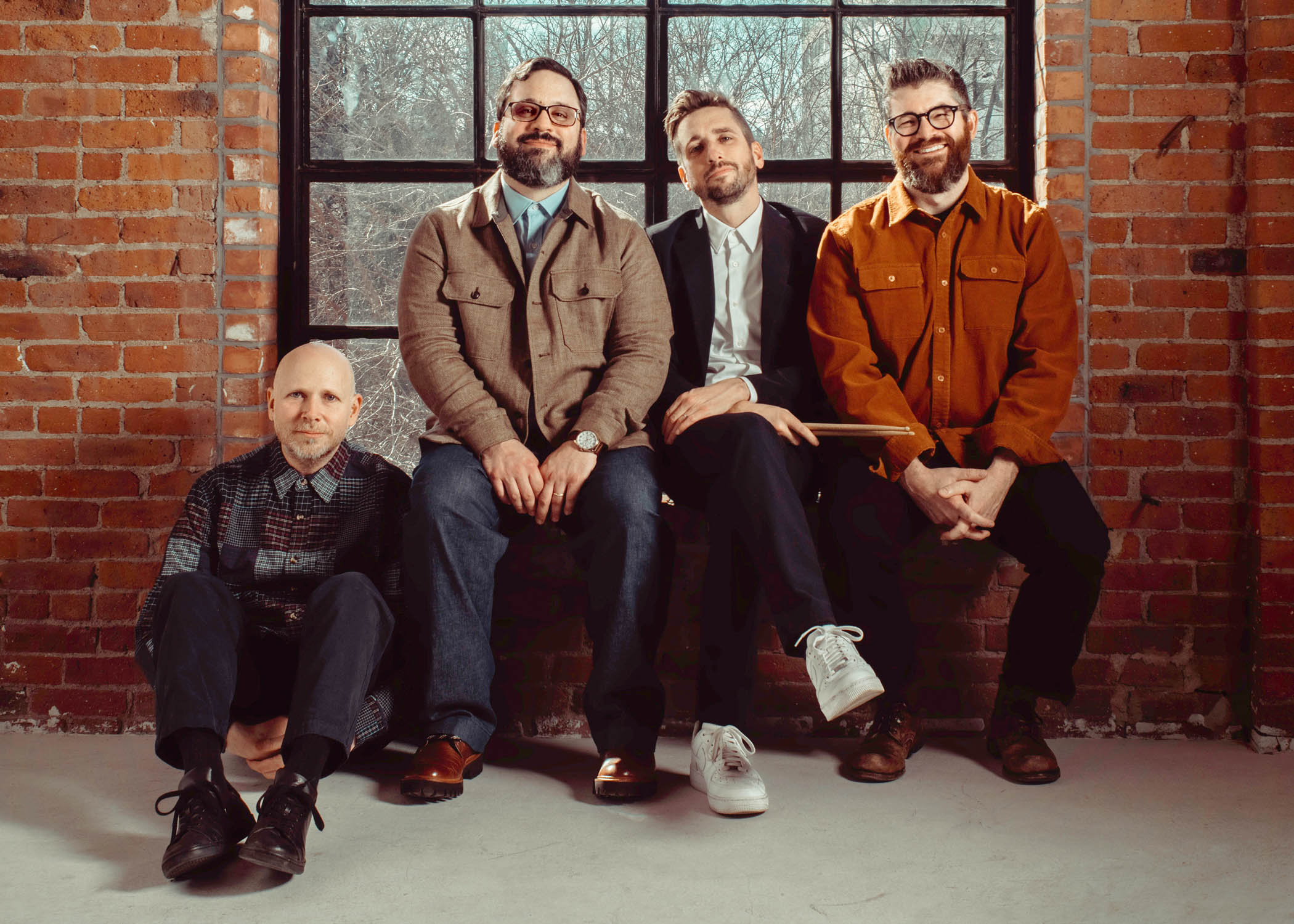 the 4 members of SO Percussion side-by-side in front of a window on a brick wall